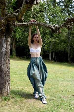 Woman wearing a white bralette and oversized green trousers posing outdoors beneath a tree branch styled by Helga Burrill