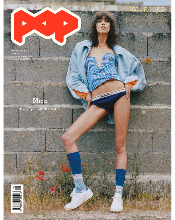 Magazine cover features a slender fashion model in a blue top and briefs, set against a grey brick wall with scattered red poppies.