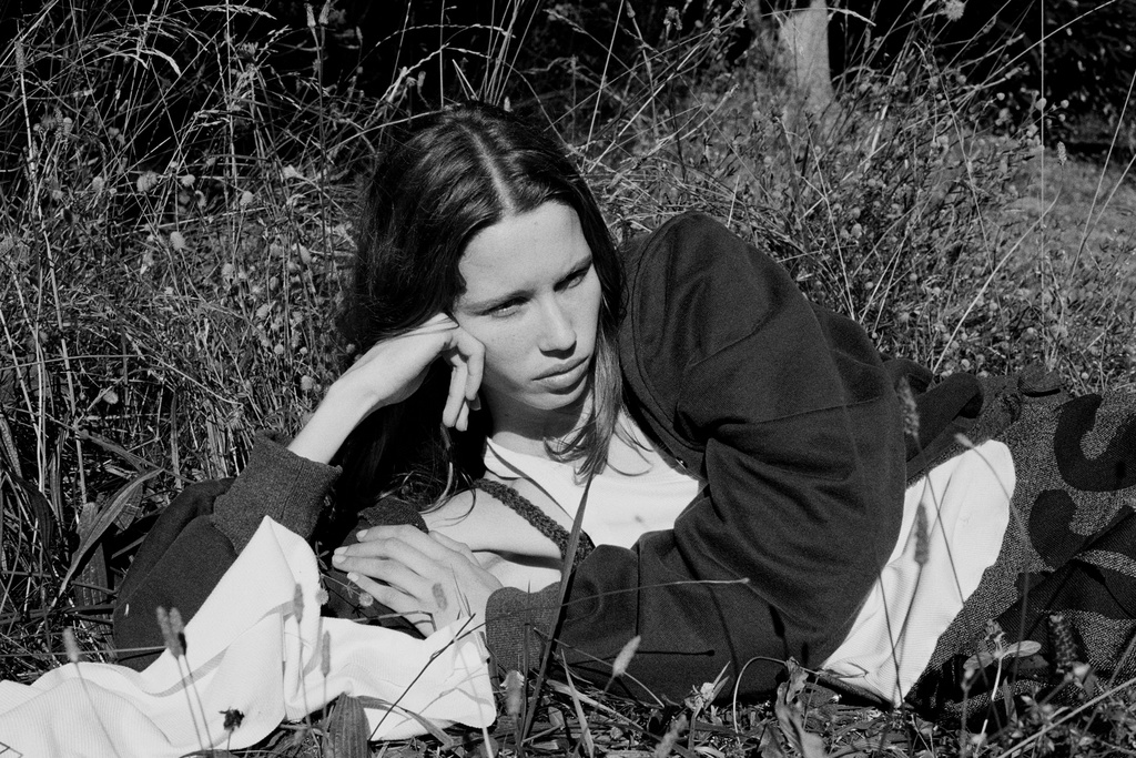 Monochrome fashion editorial image of a young woman resting her head on her hand while lying in tall wild grass.