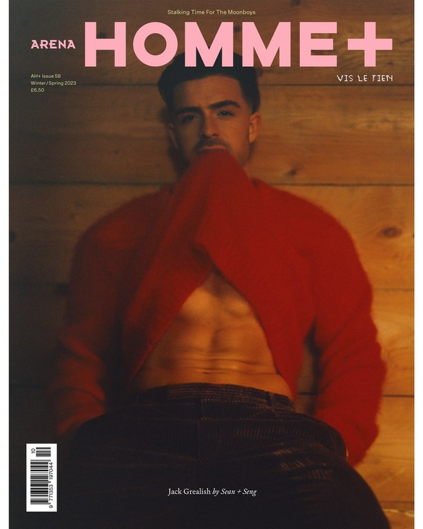 Arena Homme+ magazine cover featuring a shirtless adult male with an open red sweater posing against a wood panel background.