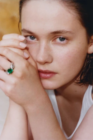 Close-up portrait of a woman wearing a white top and a large green gemstone ring, styled by Helga Burrill.