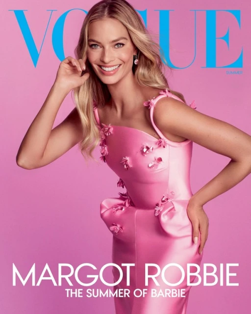 Margot Robbie is featured on a Vogue magazine cover, smiling and wearing a pink floral dress against a pink background.