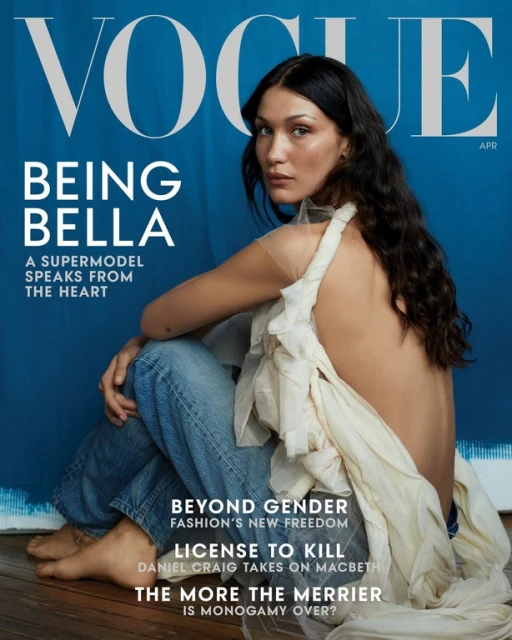 Vogue cover featuring Bella Hadid, seated in jeans and a white garment, against a textured blue background with magazine title and cover text.