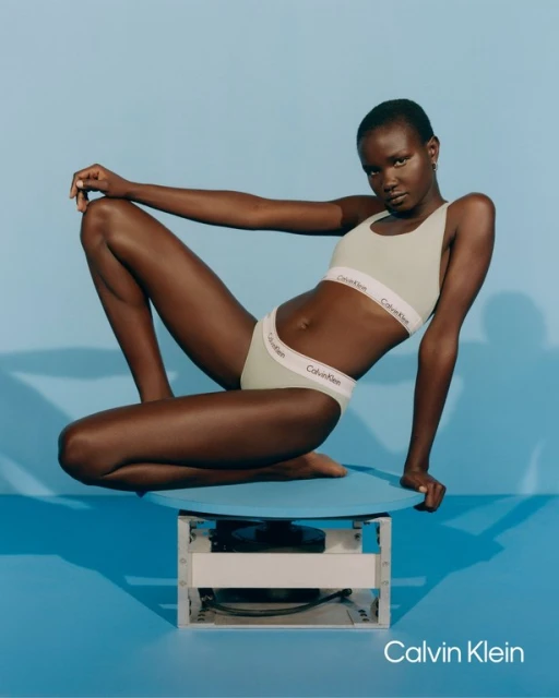 Athletic dark-skinned woman in Calvin Klein lingerie, posing in a brightly lit studio with a vibrant blue backdrop. Fashion and beauty shot.
