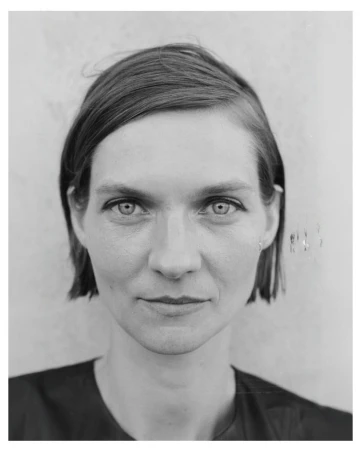 Portrait of a woman with dark short hair and a neutral expression against a plain background