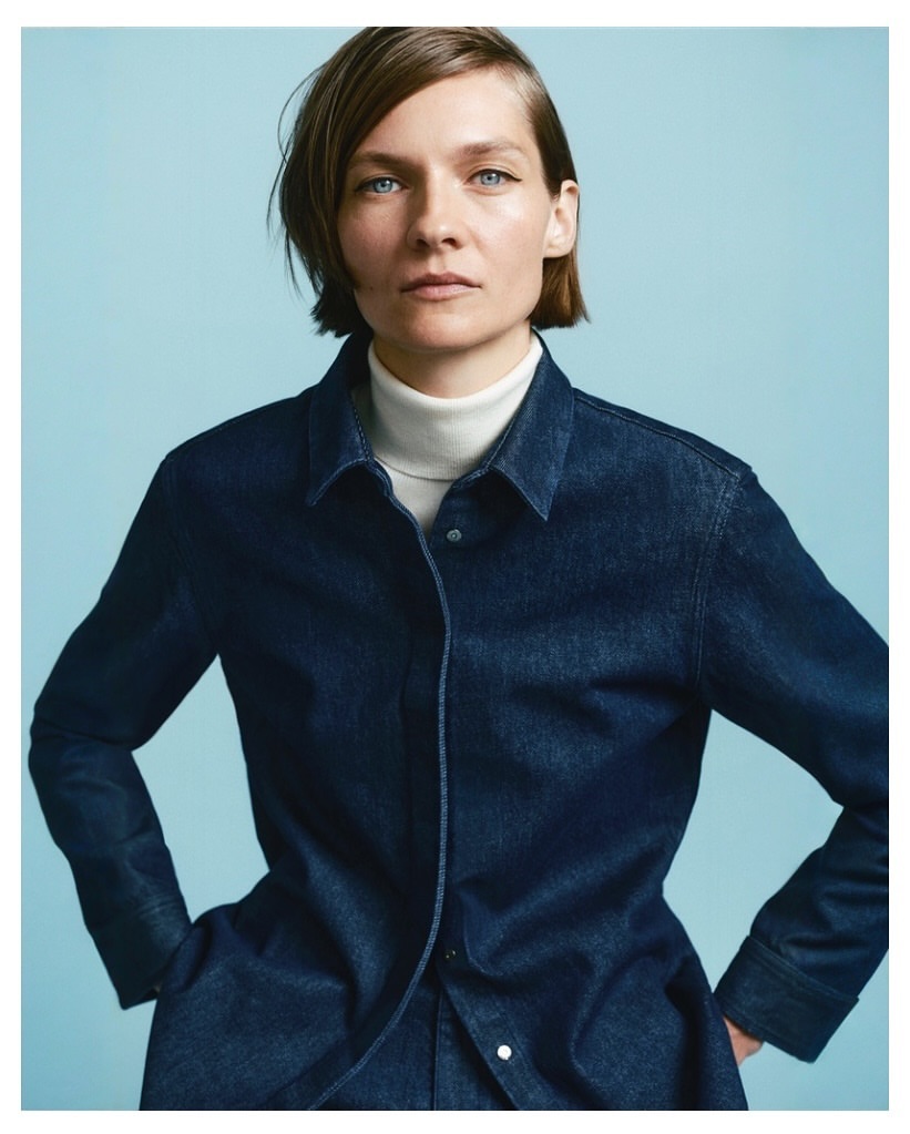Model with short brown hair wearing a dark blue denim shirt and white turtleneck against a light blue background