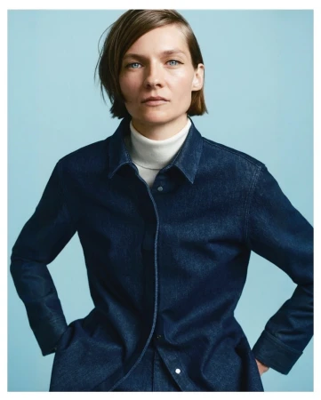 Model with short brown hair wearing a dark blue denim shirt and white turtleneck against a light blue background