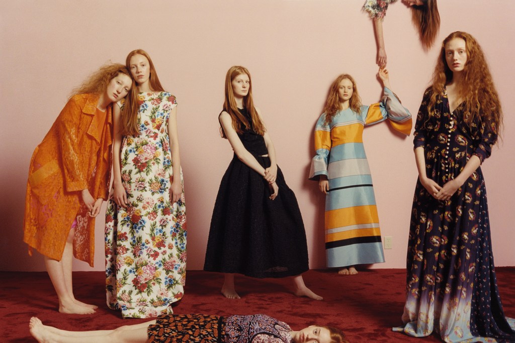 Group of red-haired models in colorful gowns and dresses posing in a photo studio against a pink background with a red carpet.