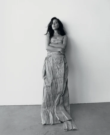Monochrome portrait of a woman in a strapless draped gown leaning against a plain wall styled by Max Ortega