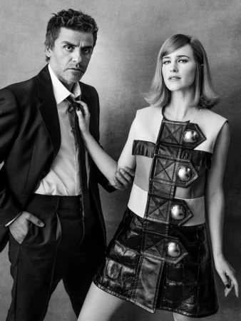 Black and white portrait of a stylish man in a suit and a woman in a dress with hardware, standing close together in a photo studio.
