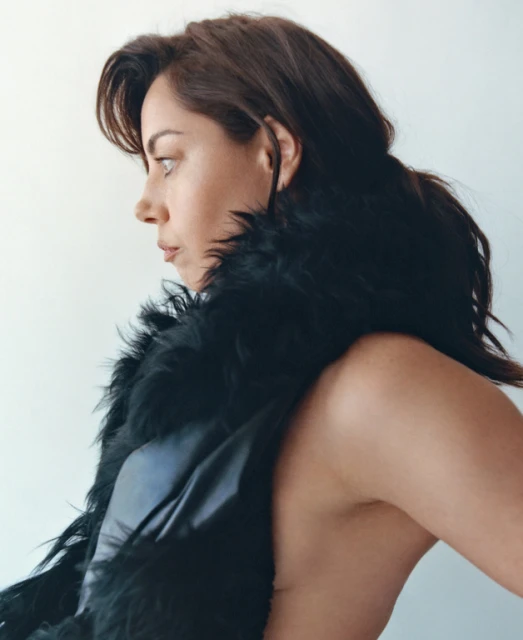 Portrait of an adult female in a black, feathered garment in a side view against a light background, fashion, celebrity, beauty