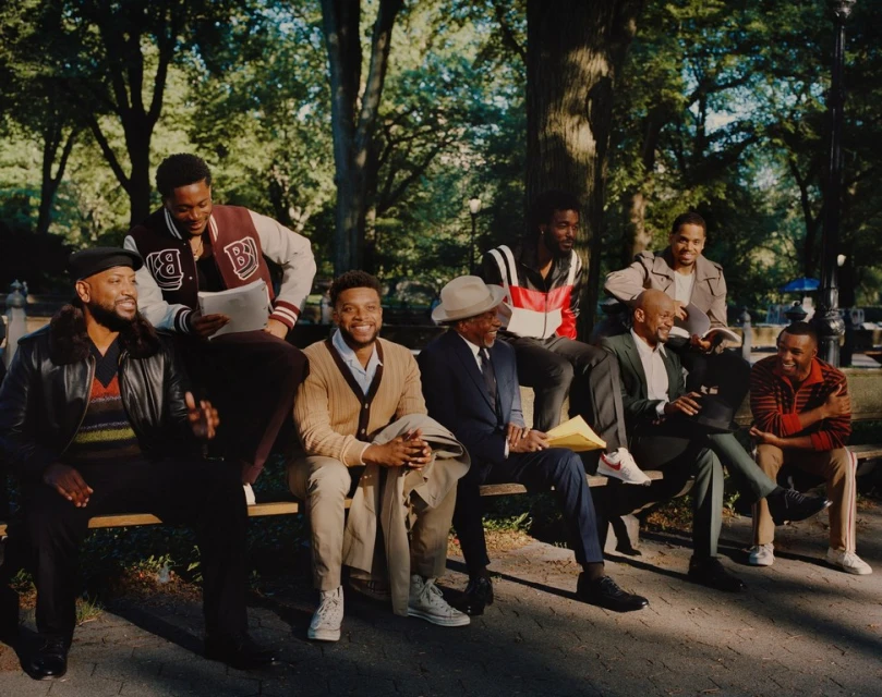 A group of African-American men sit on a bench in a sunny park, wearing a variety of fashionable clothing, creating a lifestyle editorial image.