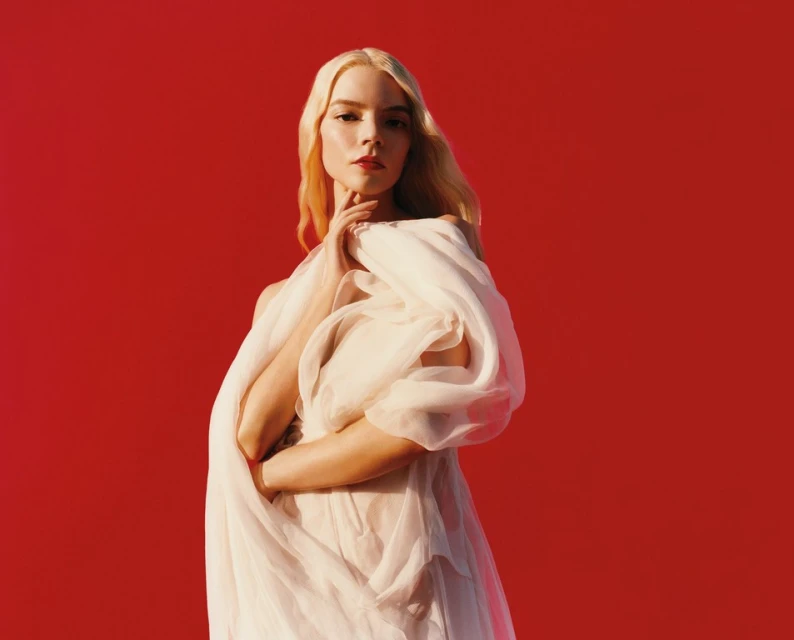 Anya Taylor-Joy poses in a flowing white gown against a vibrant red backdrop, illuminated by soft, directional lighting for a fashion editorial shot.
