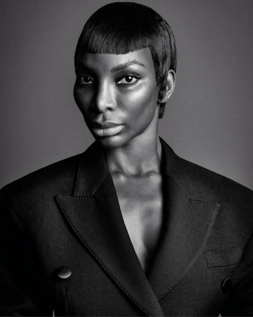 Monochrome portrait of a Black woman with short hair and a black blazer against a plain background in a studio setting.