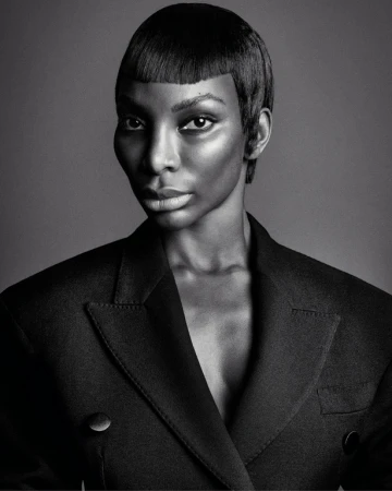 Monochrome portrait of a Black woman with short hair and a black blazer against a plain background in a studio setting.