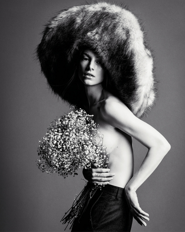 Monochrome fashion portrait of a model wearing an oversized fluffy hat and holding a bouquet of baby's breath flowers.