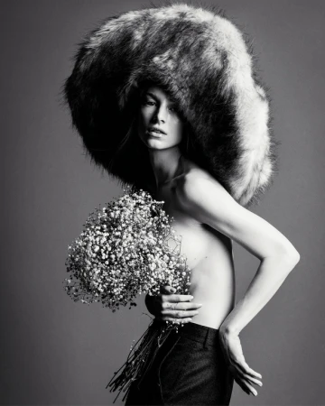 Monochrome fashion portrait of a model wearing an oversized fluffy hat and holding a bouquet of baby's breath flowers.