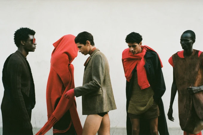 Fashion editorial showcasing five dark-haired adult models in draped and layered clothing against a stark white background.