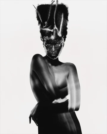 Black woman with sculpted hair adorned with fish skeletons wearing dark makeup against a plain white background