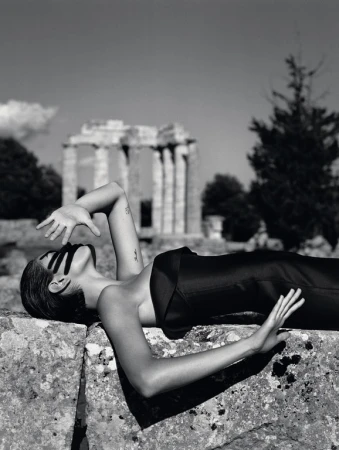 Monochromatic shot of a woman reclining on a stone structure in a black outfit, with a partial building visible in the background.