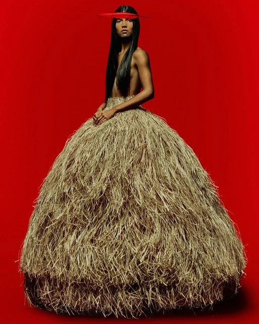 Woman in textural beige dress with red bar across eyes poses against a red background in a studio shot. Editorial fashion.