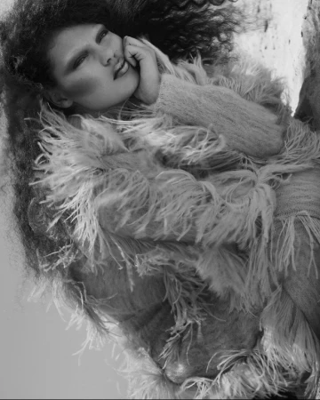 Model with voluminous dark curly hair wearing a feathered textured coat styled by Kate Phelan in a monochrome portrait.
