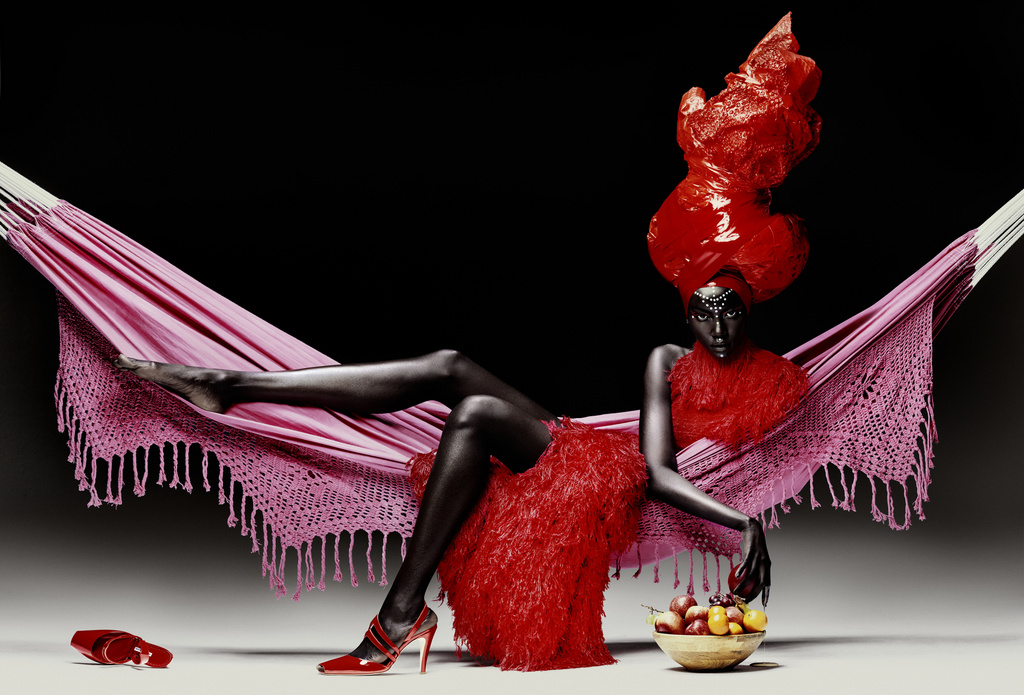 A striking image features a dark-skinned woman reclining in a pink hammock against a black backdrop, adorned in a red dress and elaborate headpiece.