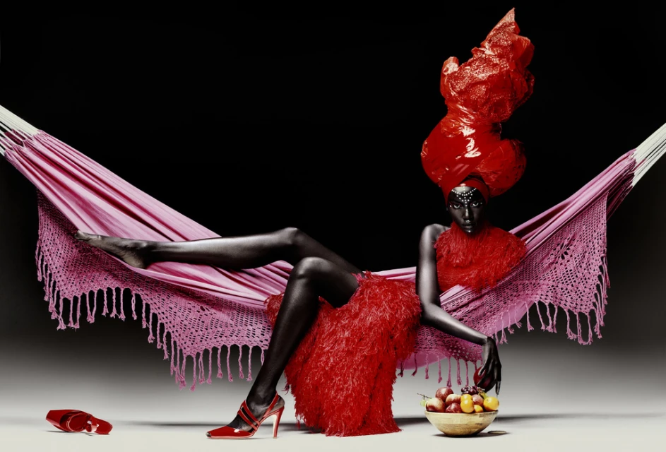 A striking image features a dark-skinned woman reclining in a pink hammock against a black backdrop, adorned in a red dress and elaborate headpiece.