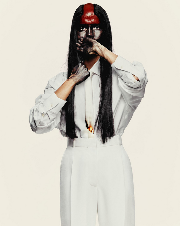 Model with painted face and red mark on forehead wearing white shirt and trousers