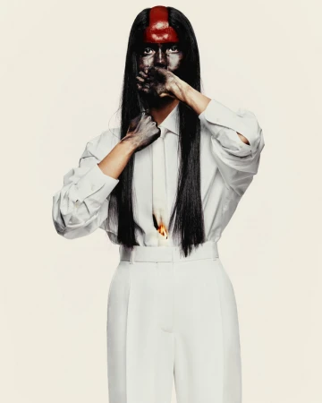 Model with painted face and red mark on forehead wearing white shirt and trousers
