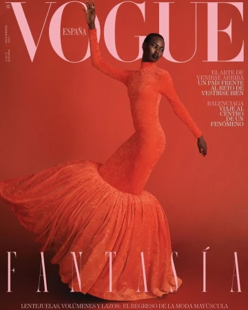 Fashion magazine cover featuring a Black female model in a long-sleeved, orange gown with a large, textured skirt against a matching backdrop.