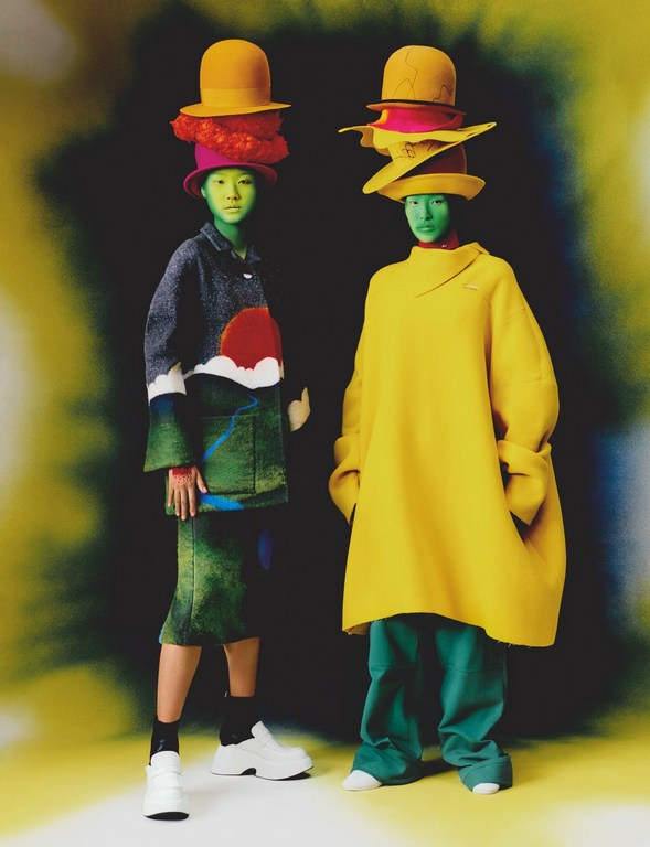 Two people in colorful hats and outfits stand side-by-side with green tinted skin, striking a pose against a dark background with yellow highlights.