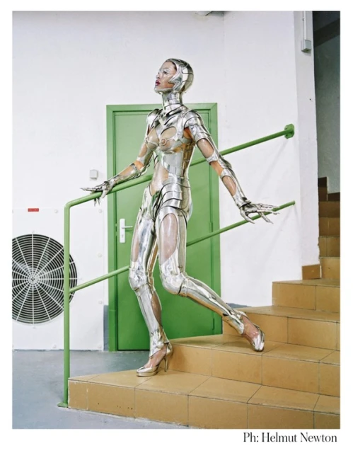 Woman in metallic futuristic armor poses on stairs indoors. Bright studio lighting captures the texture and details of the unique costume.