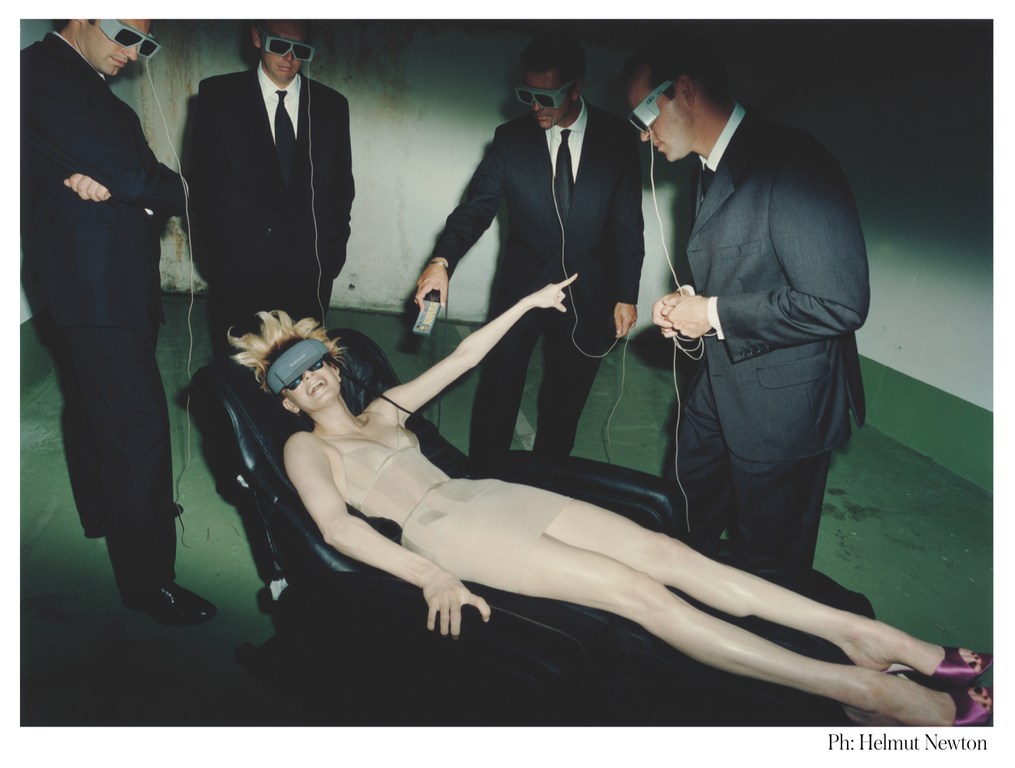 Futuristic fashion photography featuring a woman lying on a chair surrounded by men in suits and VR headsets in a stark setting.