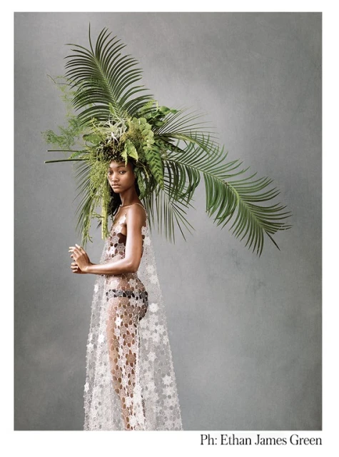 Fashion portrait of a woman wearing a sheer floral dress and an elaborate headpiece made of green foliage and palm leaves.