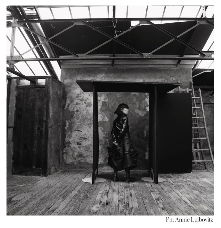 Black and white fashion shot: a woman stands in front of a black architectural structure, captured in an industrial-style room, ladder in the background.