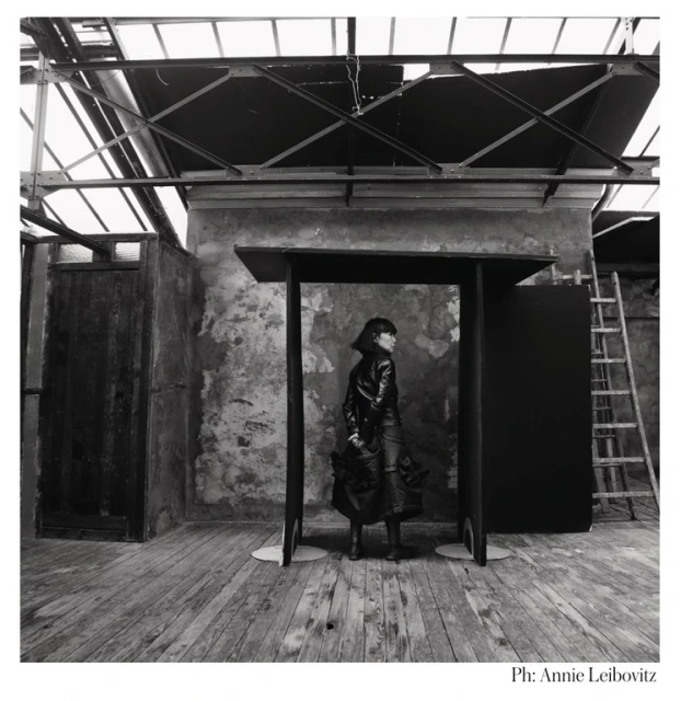 Black and white fashion shot: a woman stands in front of a black architectural structure, captured in an industrial-style room, ladder in the background.