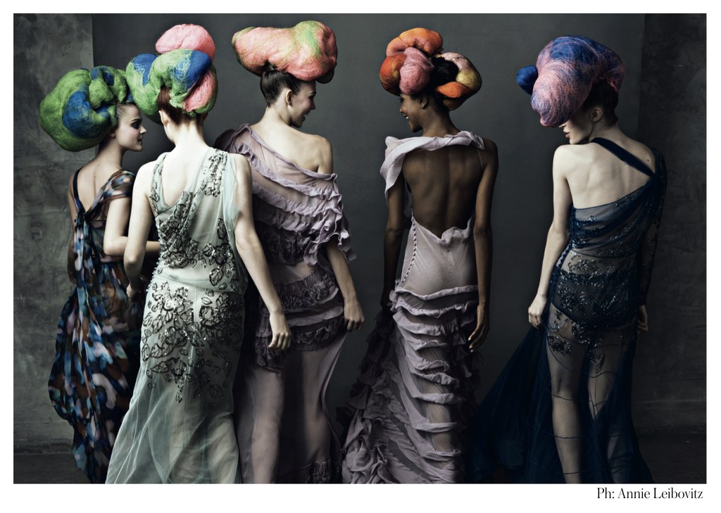 Five women pose indoors, showcasing couture gowns and voluminous, colorful hairstyles against a neutral backdrop in a fashion editorial.