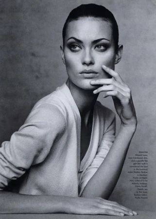 Monochromatic portrait of a woman with slicked-back hair wearing a v-neck top, gazing to the side with her hand near her face.