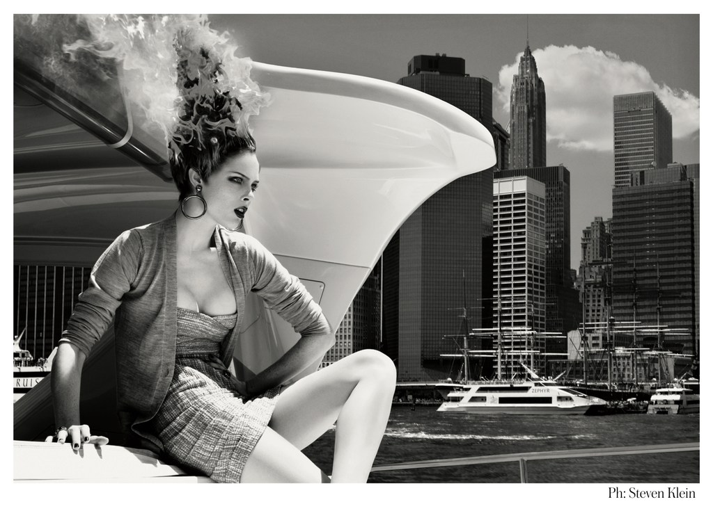 Black and white fashion shot features a woman sitting atop a white vehicle with a cityscape backdrop, creating a dramatic editorial scene.