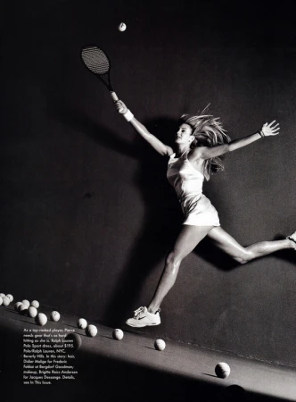 Black and white fashion editorial photograph of a female tennis player leaping in mid-air against a dark background with tennis balls