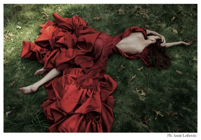 Woman wearing a voluminous red silk dress lying barefoot on grass with scattered leaves, styled by Phyllis Posnick.