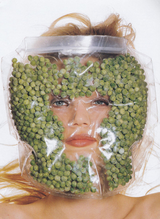 Conceptual close-up studio shot of a female model wearing a clear plastic bag filled with green peas over her head and face.