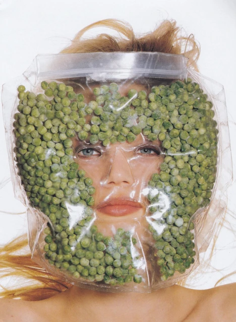 Conceptual close-up studio shot of a female model wearing a clear plastic bag filled with green peas over her head and face.