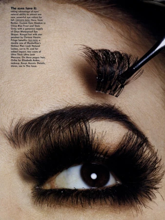 Close-up of a person's eye with very long, dramatic false eyelashes being applied with a cosmetic brush for a beauty campaign.
