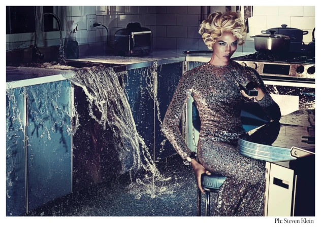 Blonde woman in a sequin gown poses in a kitchen with overflowing water. Fashion and editorial photography create a surreal scene.