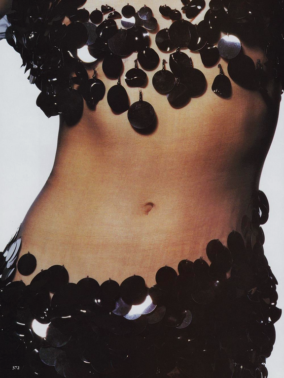 Close-up of a slender adult woman's torso adorned with glittering black disc embellishments on a white background.