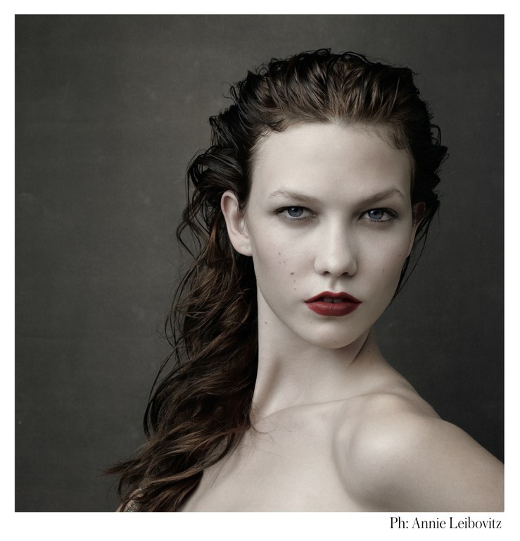 Portrait of a woman with dark hair, fair skin, and red lips posing against a dark background in a photo by Annie Leibovitz.