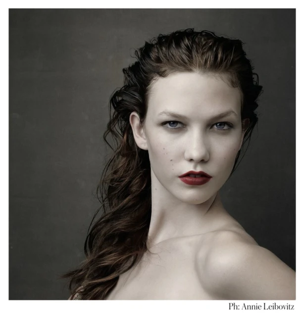 Portrait of a woman with dark hair, fair skin, and red lips posing against a dark background in a photo by Annie Leibovitz.