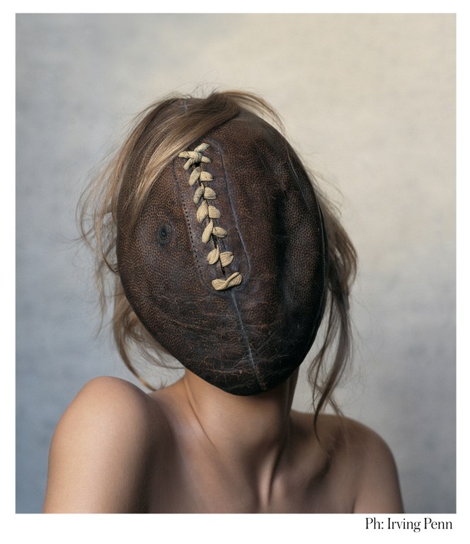 Conceptual portrait of a topless adult female with blond hair, her face obscured by a brown leather American football.